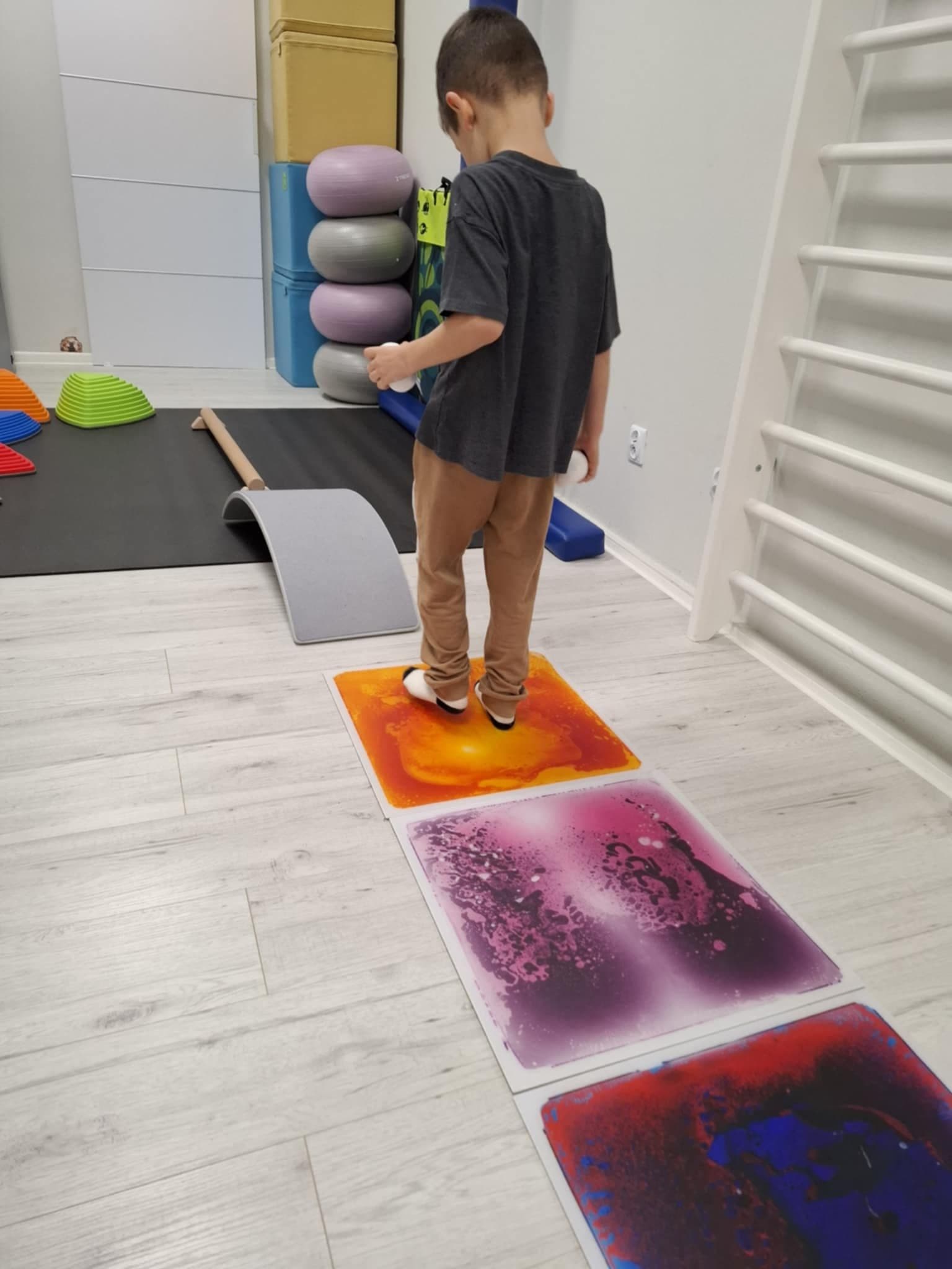 Chłopiec chodzi po matach wypełnionych kolorową cieczą podczas terapii integracji sensorycznej