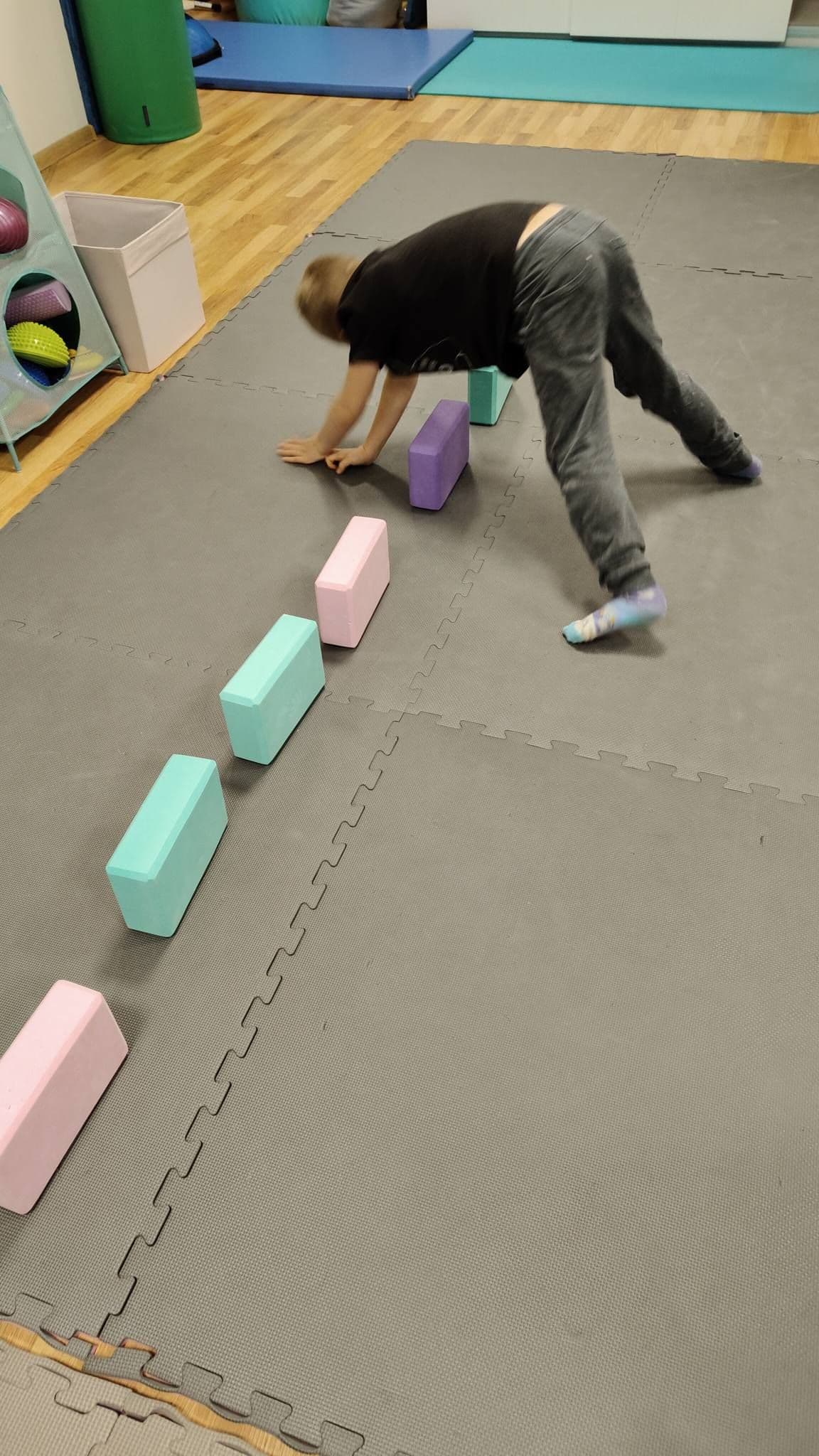 Chłopiec porusza się w pozycji podporu omijając kostki do jogi podczas terapii ręki 