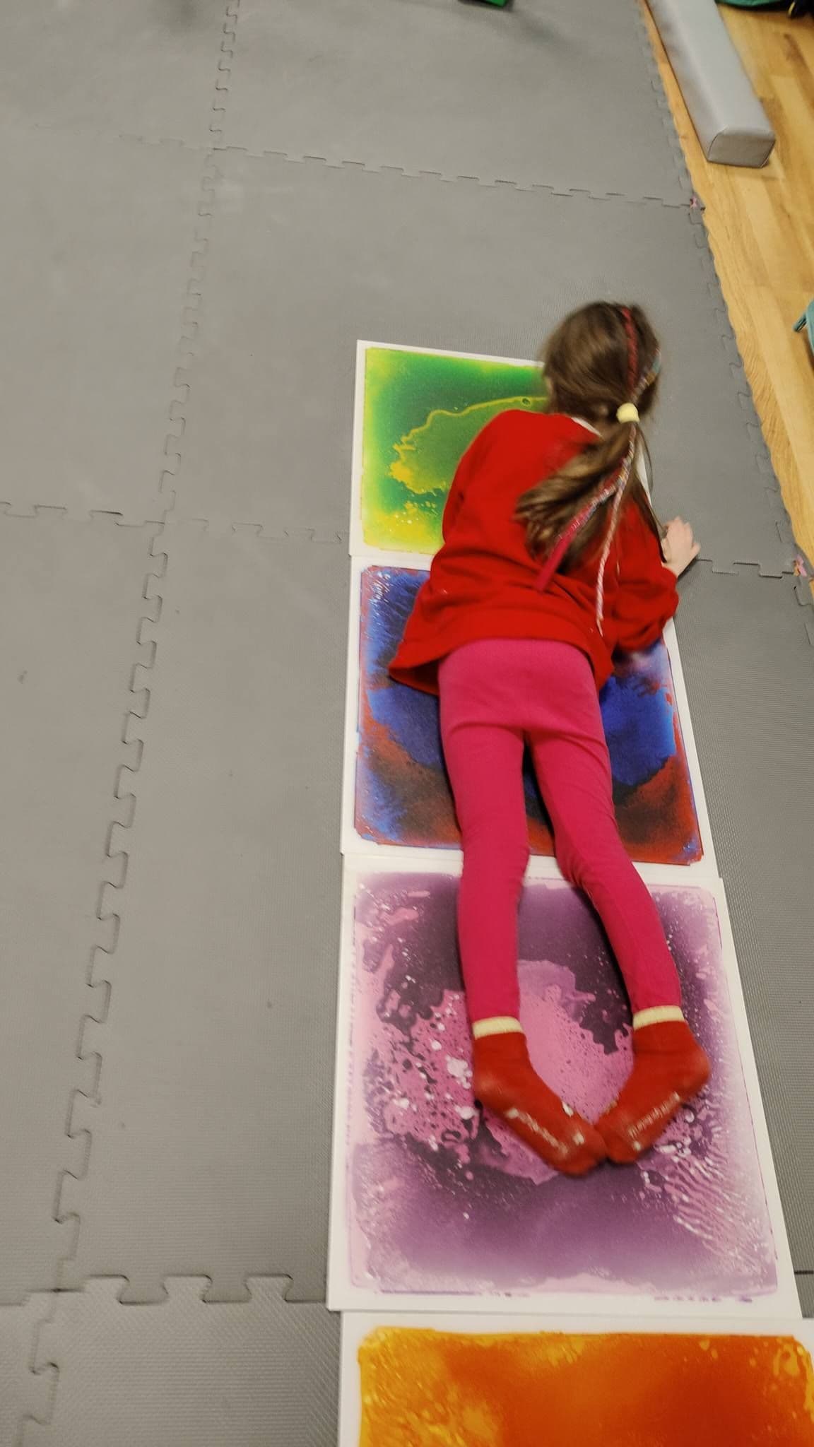 Dziewczynka czołga się po kolorowych matach podczas fizjoterapii